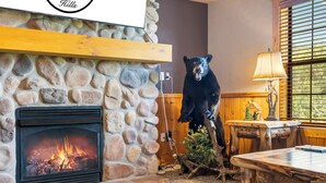 A fireplace with a stone surround, a bear statue, a wooden table, and a lamp. - Spacious Cabin in the Heart of Branson, near shows, shopping! (Branson)