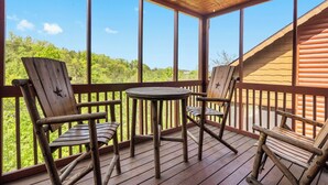 A wooden deck with a table and chairs, overlooking a forested area. - Spacious Cabin in the Heart of Branson, near shows, shopping! (Branson)