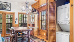A rustic cabin interior with a wooden dining table, a chandelier, and a washing machine.
