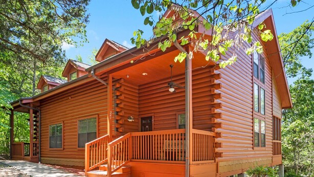 A log cabin with a porch, multiple windows, and a chimney.