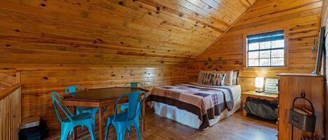 Een knus houten kamer met een houten plafond, een bed met quilt, een tafel met stoelen en een raam.