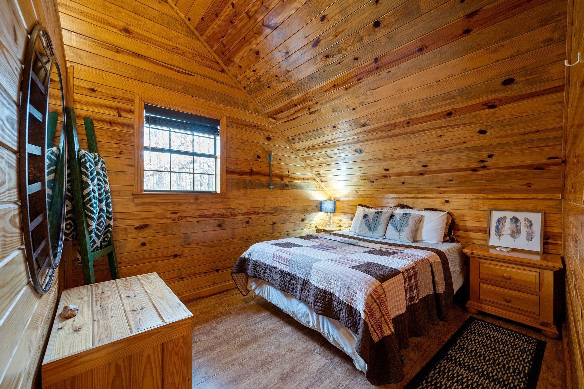 A wooden cabin bedroom with a bed, nightstand, dresser, window, and a ladder.