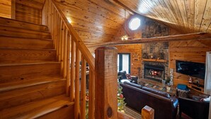 Ein Holzinnenraum mit Treppe, Kamin und Wohnbereich mit Sofa und Fernseher.