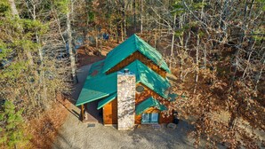 Eine Hütte mit grünem Dach, Stein Fundament und Holz Wänden, umgeben von einem Wald.