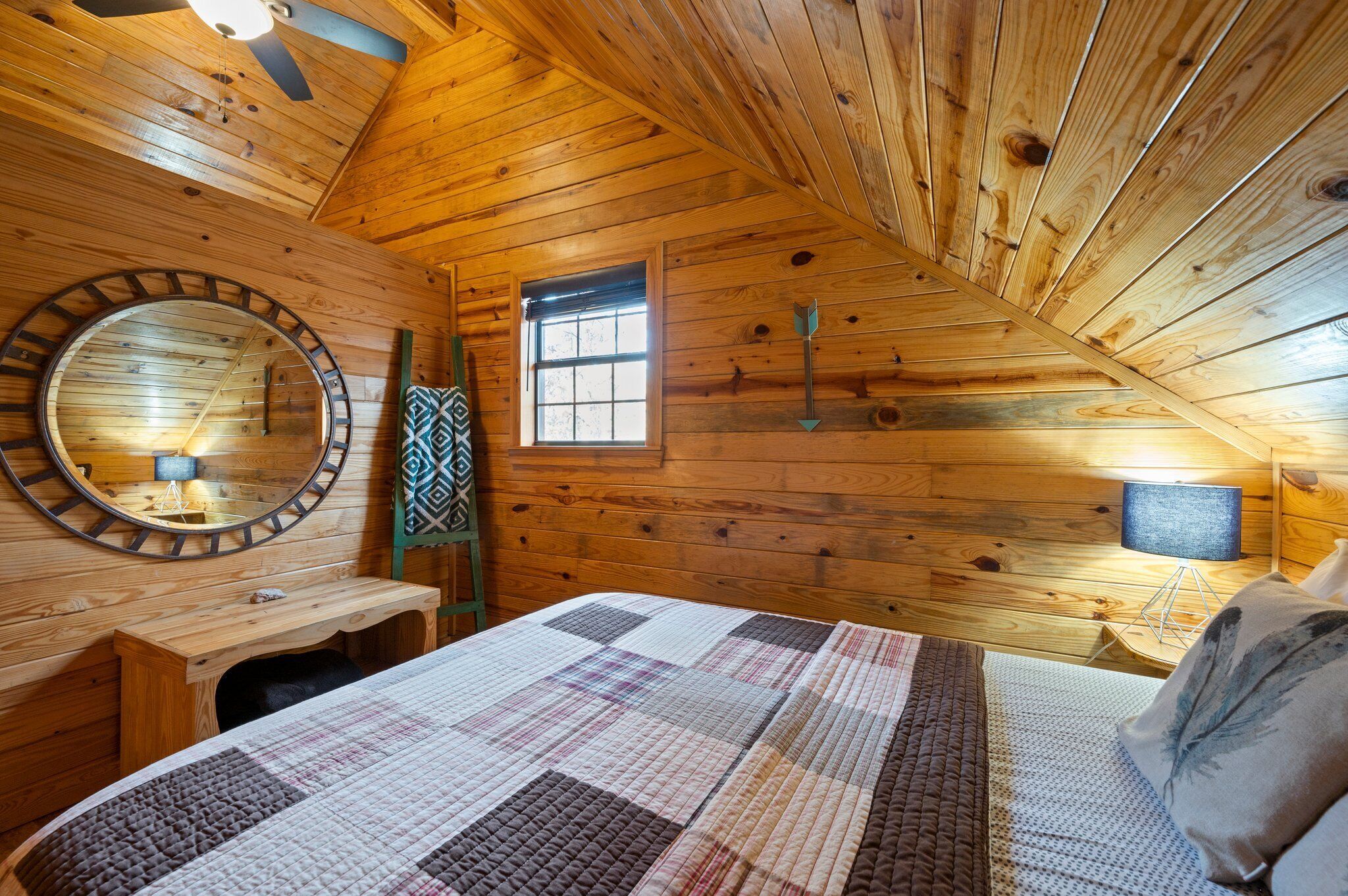 Een gezellig slaapkamer in een houten hutje, met een groot bed, een ronde spiegel, een klein raam en een houten plafond.