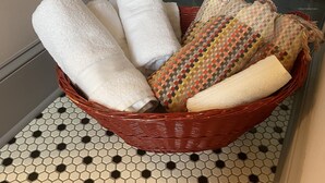 A corner of a bathroom with a tiled floor, a white towel, and a basket with towels and a patterned cloth.