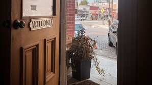 A wooden door with a 'WELCOME' sign, a potted plant, and a view of a street with cars and buildings.