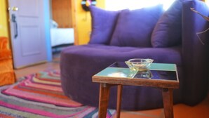 A room with a purple sofa, a glass table with a bowl, and a colorful rug. - Groovy Desert Getaway w Pool, Fire pit, Stream/Wifi, Vinyl Records, Books, Art.. (Twentynine Palms)