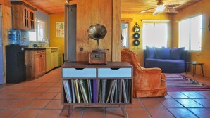 A cozy living room with a wooden ceiling, a blue sofa, and a record player on a wooden cabinet. - Groovy Desert Getaway w Pool, Fire pit, Stream/Wifi, Vinyl Records, Books, Art.. (Twentynine Palms)