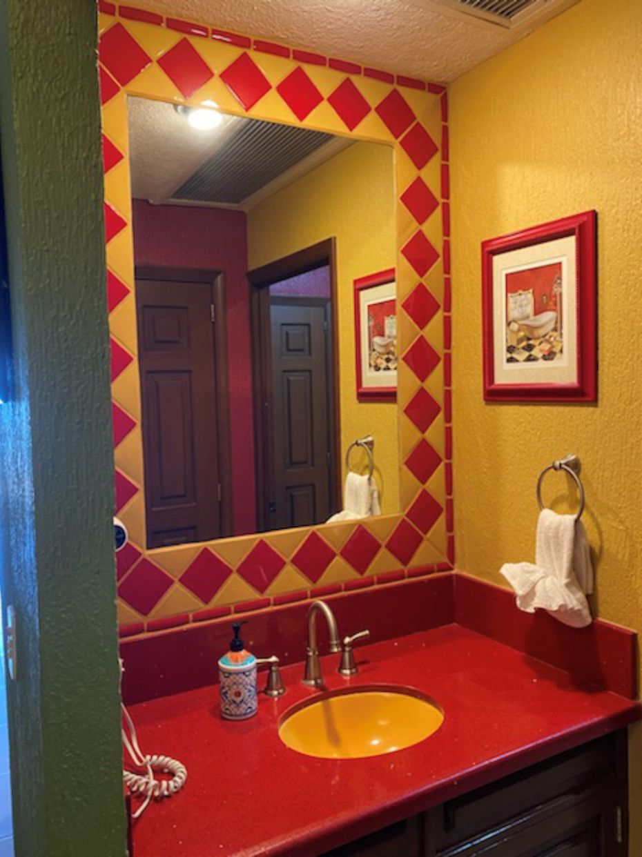 A bathroom with a red sink, yellow walls, and a mirror with a diamond pattern.