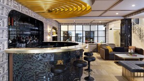 A modern bar area with a curved counter, bar stools, and a seating area with sofas and a coffee table. - The Alest Hotel (Mexico City)