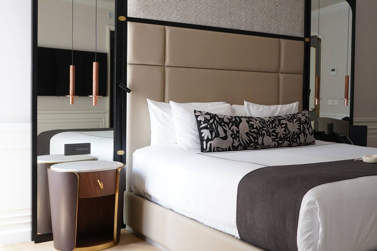 A modern bedroom with a large bed, a bedside table, a mirror, and a wardrobe.