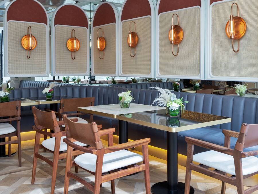 En restaurang med trästolar och träbord, ett fiskbensmönstrat golv och ett tak med synliga takbjälkar.
