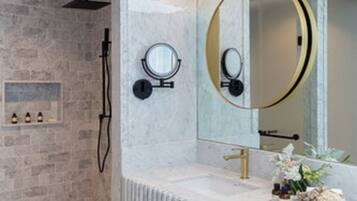 A modern bathroom with a marble vanity, a large mirror, and a shower area with a stone wall.