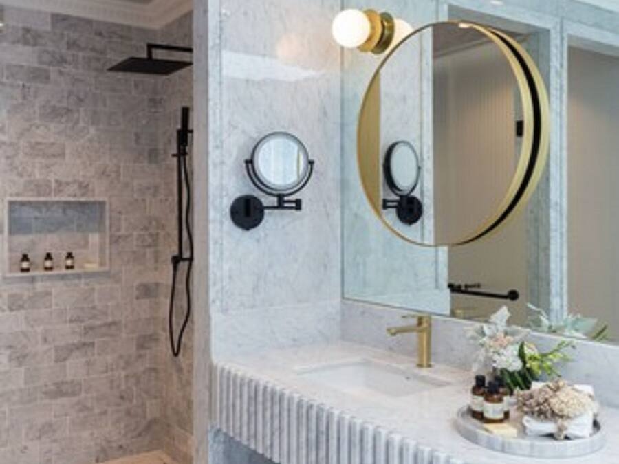 A modern bathroom with a marble vanity, a large mirror, and a shower area with a stone wall.