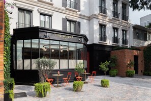 A hotel with a glass facade, outdoor seating area, and a brick wall.