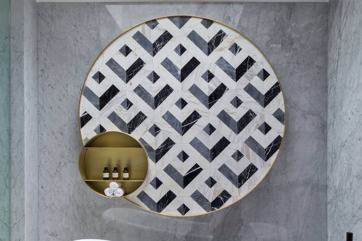 A bathroom with a freestanding bathtub, a circular wall decoration, and a gold shelf with toiletries.