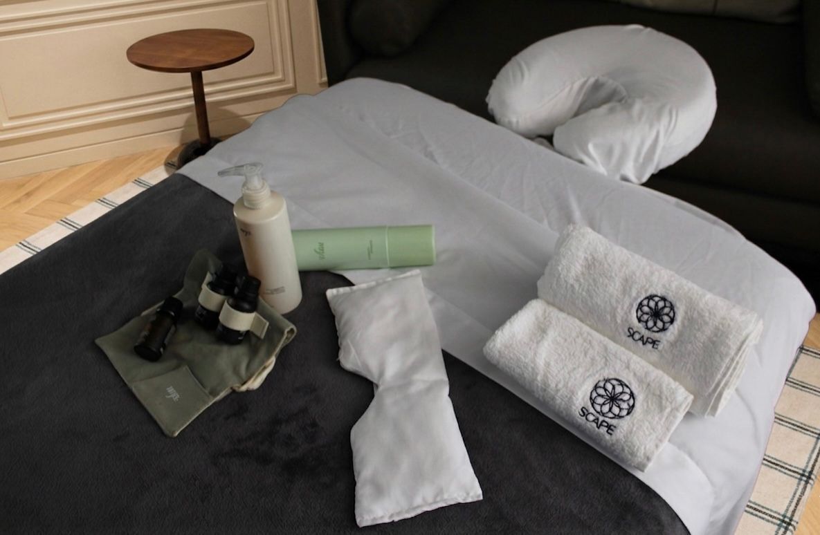 A neatly made bed with white pillows and a blanket, a small round table, and toiletries on the bed.