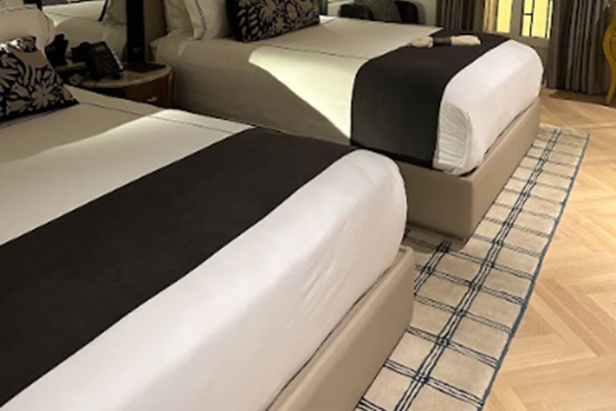 A hotel room with two beds, a large mirror, a bedside table, and a view of the outdoors through a window.