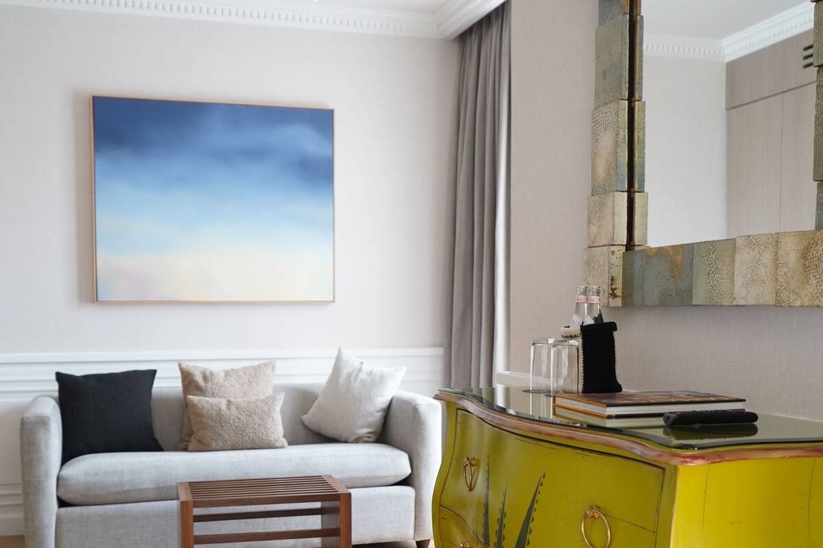 A modern living room with a light grey sofa, a yellow cabinet, and a large abstract painting on the wall.