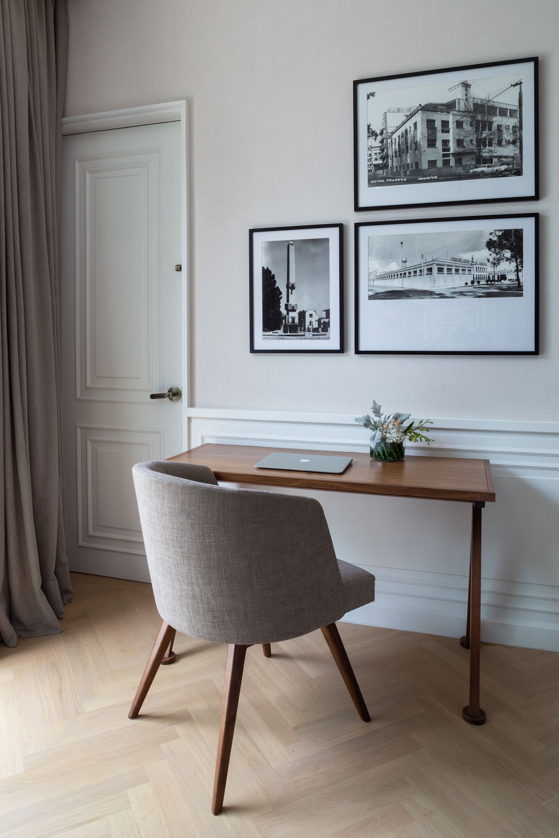 Ein Zimmer mit einem Holztisch, einem grauen Stuhl und drei gerahmten Fotos an der Wand.