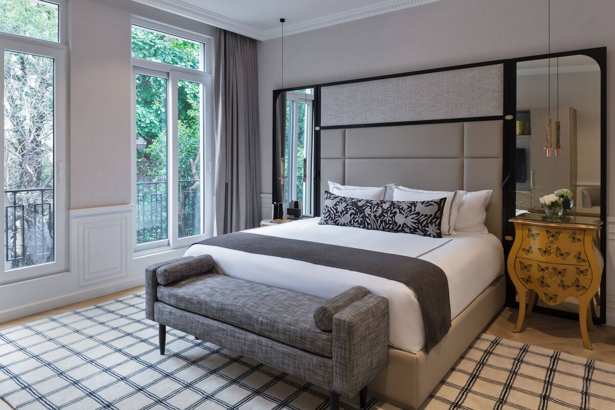 A bedroom with a large bed, a bench, a nightstand, and a mirror.