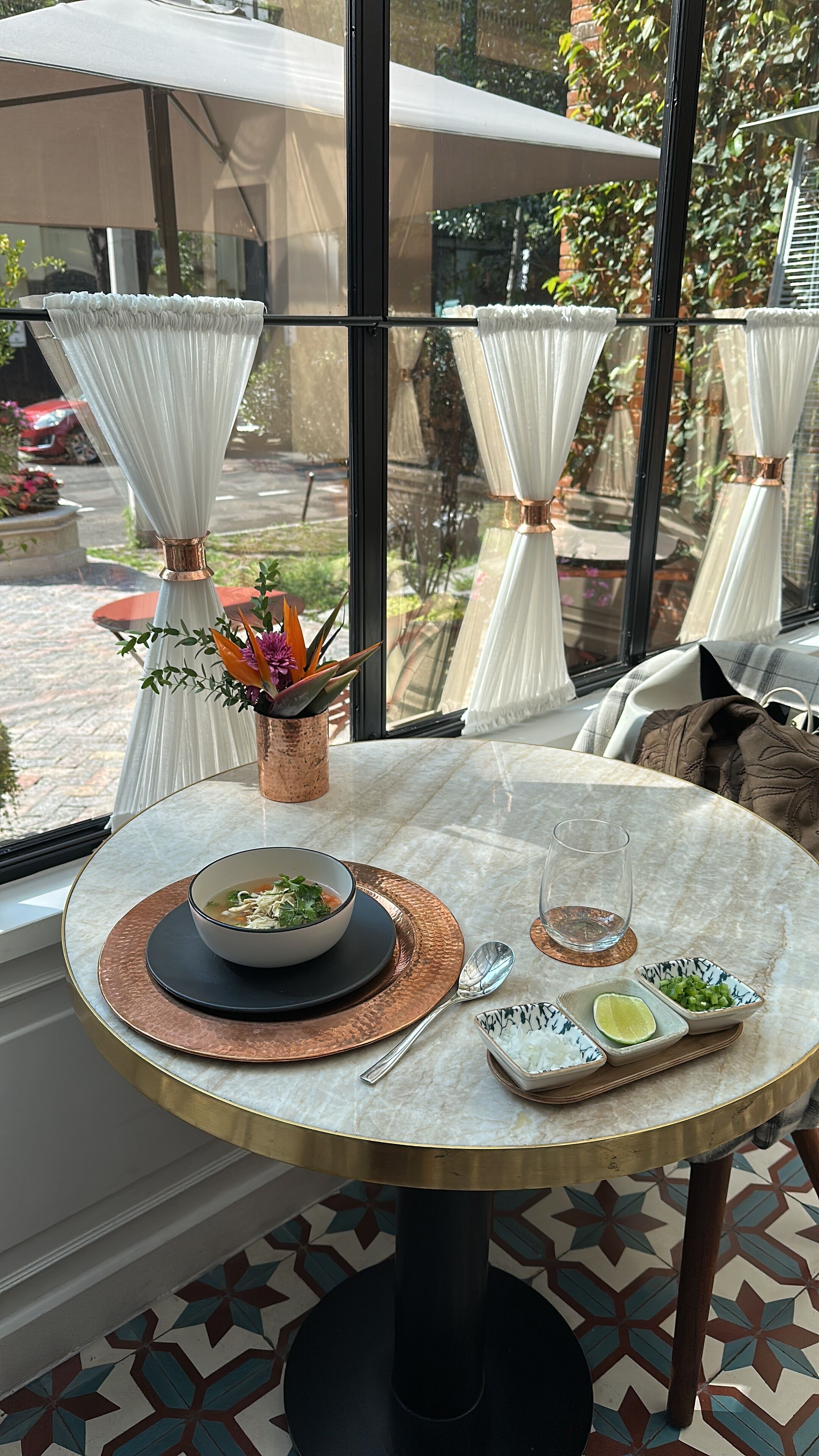 A dining table with a bowl of soup, a spoon, and small bowls of rice and lime.