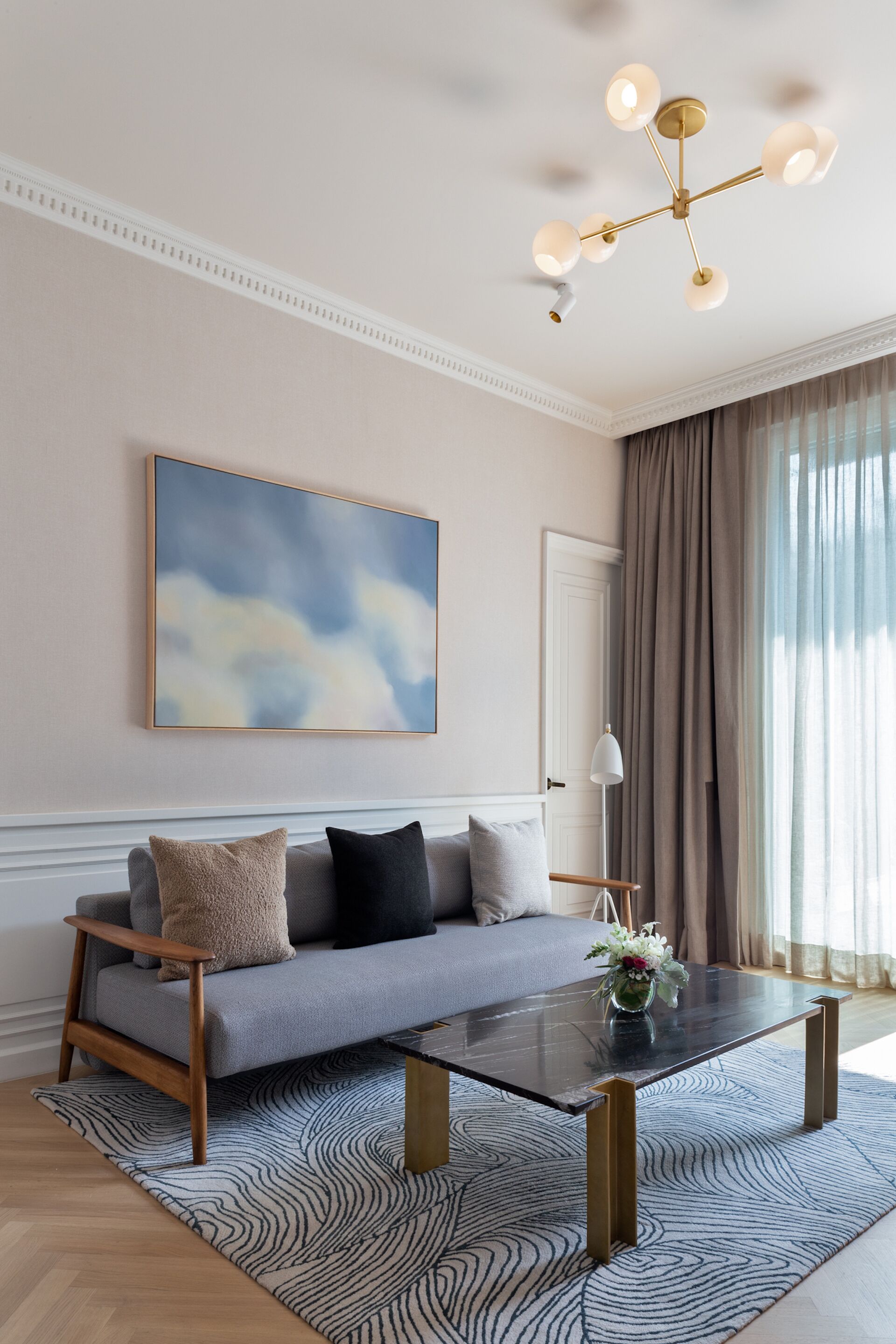 Un salon moderne avec un canapé gris, une table basse en verre et un grand tableau abstrait accroché au mur.