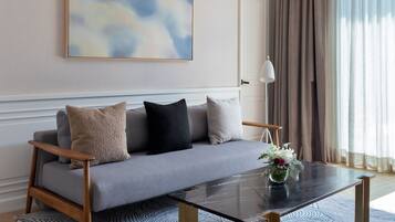 Un salon moderne avec un canapé gris, une table basse en verre et un grand tableau abstrait accroché au mur.