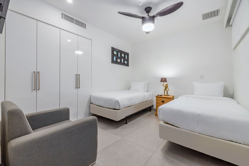A modern bedroom with two single beds, a sofa, a wardrobe, and a ceiling fan.