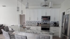 A modern kitchen with white cabinets, a marble countertop, and stainless steel appliances. There are three bar stools and a chandelier. - 4 Bedroom Pool home with pond view in Sarasota, FL (Sarasota)