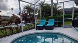 A swimming pool with two lounge chairs, surrounded by a glass enclosure with a view of palm trees and a lawn. - 4 Bedroom Pool home with pond view in Sarasota, FL (Sarasota)