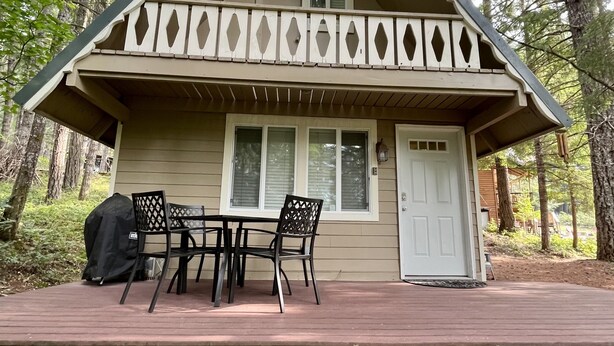 A lodge with a two-story design, featuring a balcony with lattice railings, a front door, and a covered deck area with chairs. - Timberline cabin close to Mt. Rainer and White Pass, WiFi, Netflix, AC (Packwood)