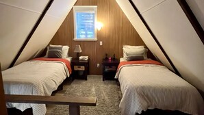 A triangular attic bedroom with two beds, a small window with blinds, and a nightstand with a lamp. - Timberline cabin close to Mt. Rainer and White Pass, WiFi, Netflix, AC (Packwood)