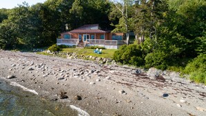 A beachfront property with a house, a covered deck, and a sandy beach. - Wings Cottage - Oceanfront! (Trenton)