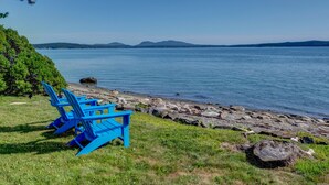 A lakeside view with blue Adirondack chairs and a rocky shoreline. - Wings Cottage - Oceanfront! (Trenton)