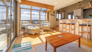 A spacious living area with a wooden table, wicker chairs, and a large window offering a view. - Wings Cottage - Oceanfront! (Trenton)
