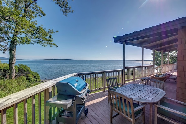 A wooden deck with a grill, outdoor seating, and a view of a lake.