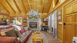 A cozy log cabin interior with a stone fireplace, wooden ceiling, and a comfortable seating area. - Location! Cute Studio Log Cabin,Hot Tub,Fireplace (Pigeon Forge)