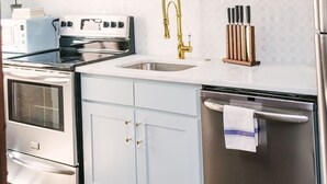 Een keuken met witte kastjes, een roestvrijstalen koelkast, een dubbele oven en een wastafel met een gouden kraan.