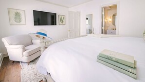 Een slaapkamer met een groot bed, een witte fauteuil, een klein tafeltje met een blauwe lamp, en lijstwerken aan de muur.