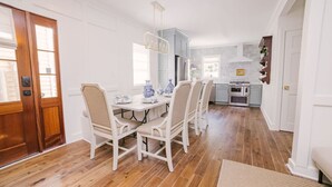 Een eetgedeelte met een houten vloer, een witte eettafel en stoelen. Achtergrond is een keuken met lichtblauwe kasten en een fornuis.