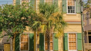 A two-story yellow building with green shutters, a palm tree in front, and a street lamp to the right. - EAST 42 C - 1 Bedroom, 1 Block to King (Charleston)