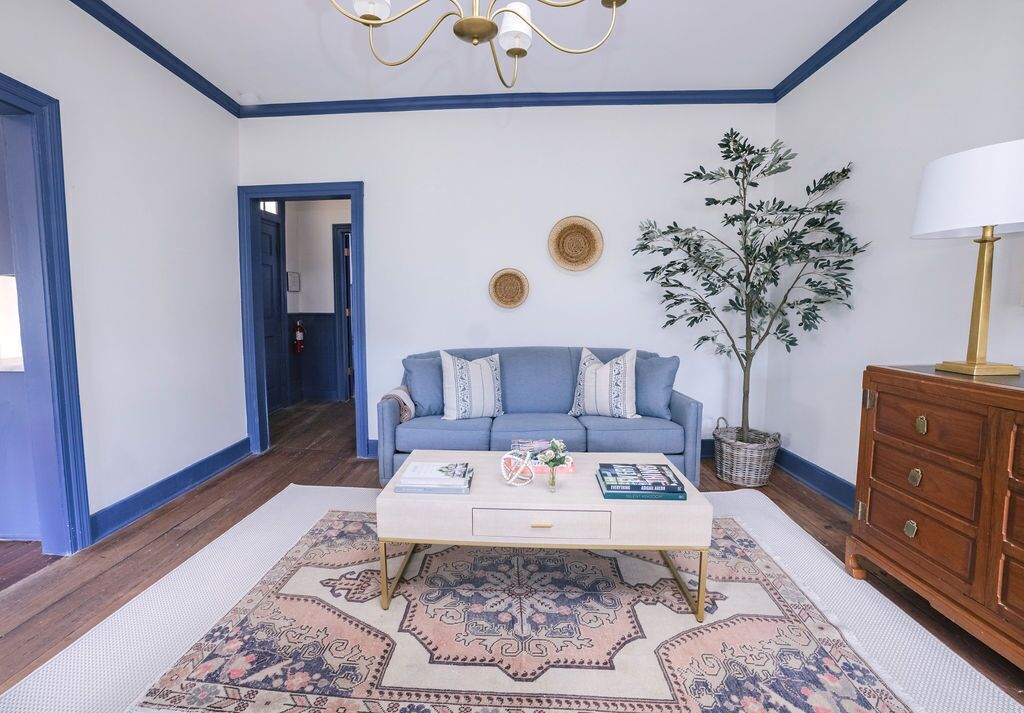 A room with a blue sofa, a white coffee table, a patterned rug, a wooden cabinet, and a potted plant.