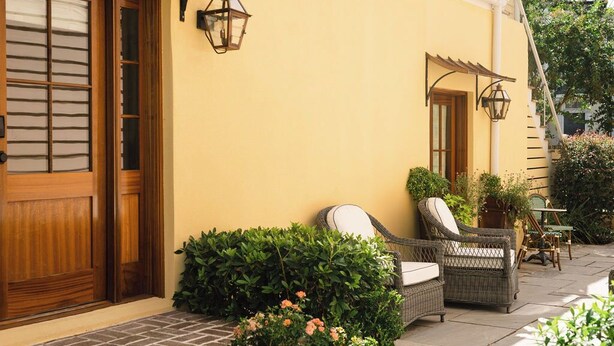 A building with a yellow facade, wooden doors, wicker furniture, and outdoor lighting. - EAST 42 C - 1 Bedroom, 1 Block to King (Charleston)