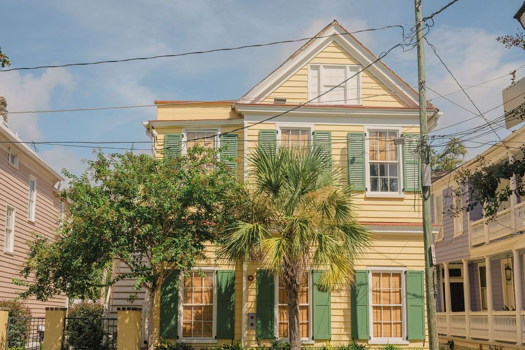 A yellow building with green shutters and a palm tree in front.