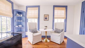 A room with two white chairs, a small round table, and a blue shelving unit with white dishes. - EAST 42 C - 1 Bedroom, 1 Block to King (Charleston)