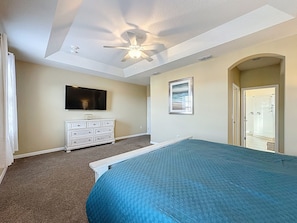A bedroom with a bed, a ceiling fan, a dresser, a TV, and a door leading to a bathroom. - Veranda Home, 8br, 6 en-suites, Lake View, POOL/SPA, FREE Resort Amenities! (Kissimmee)