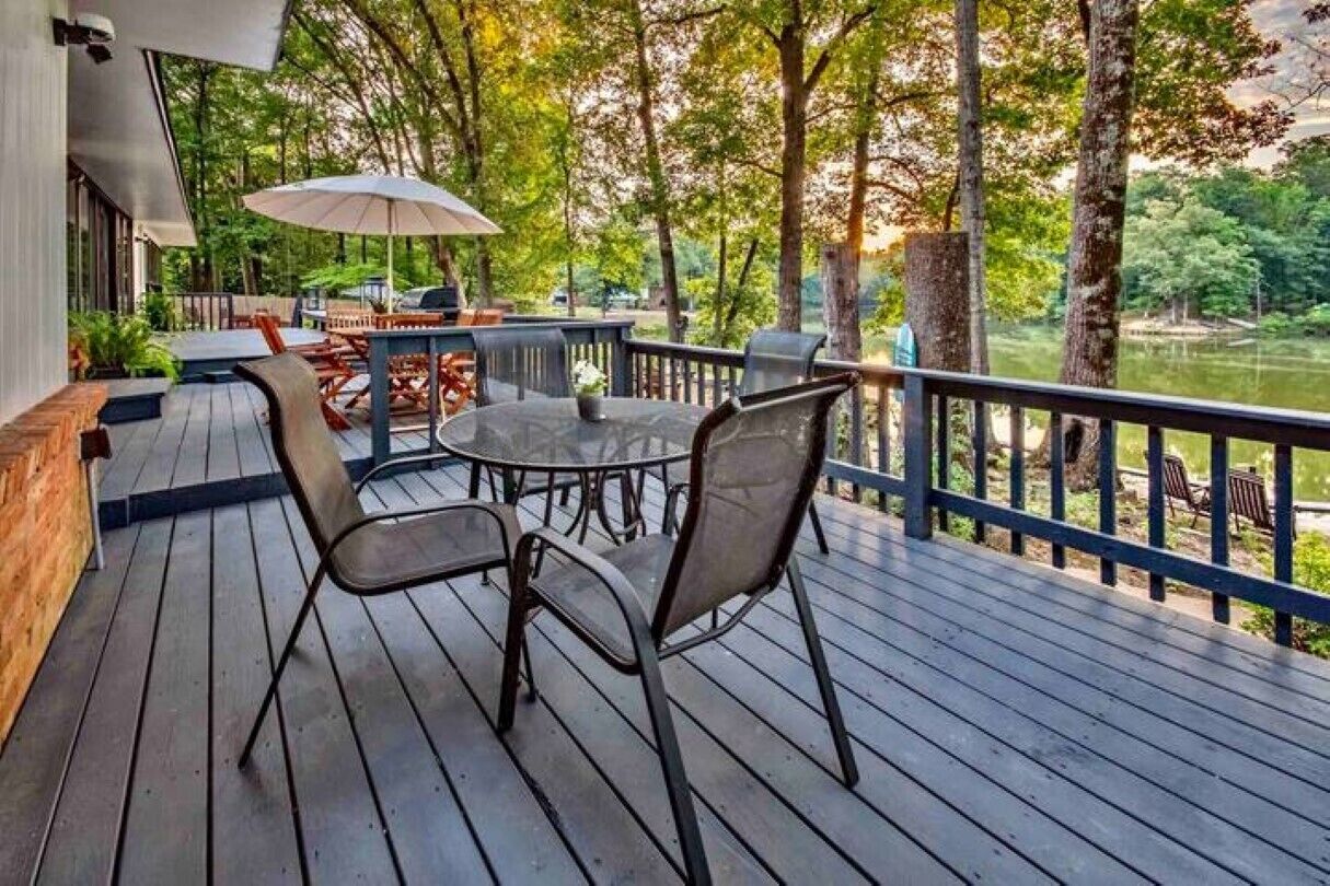 Une terrasse en bois avec une table ronde et des chaises, donnant sur un lac.
