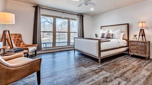 A bedroom with a large bed, a chair, a desk, and a window with a view of trees.